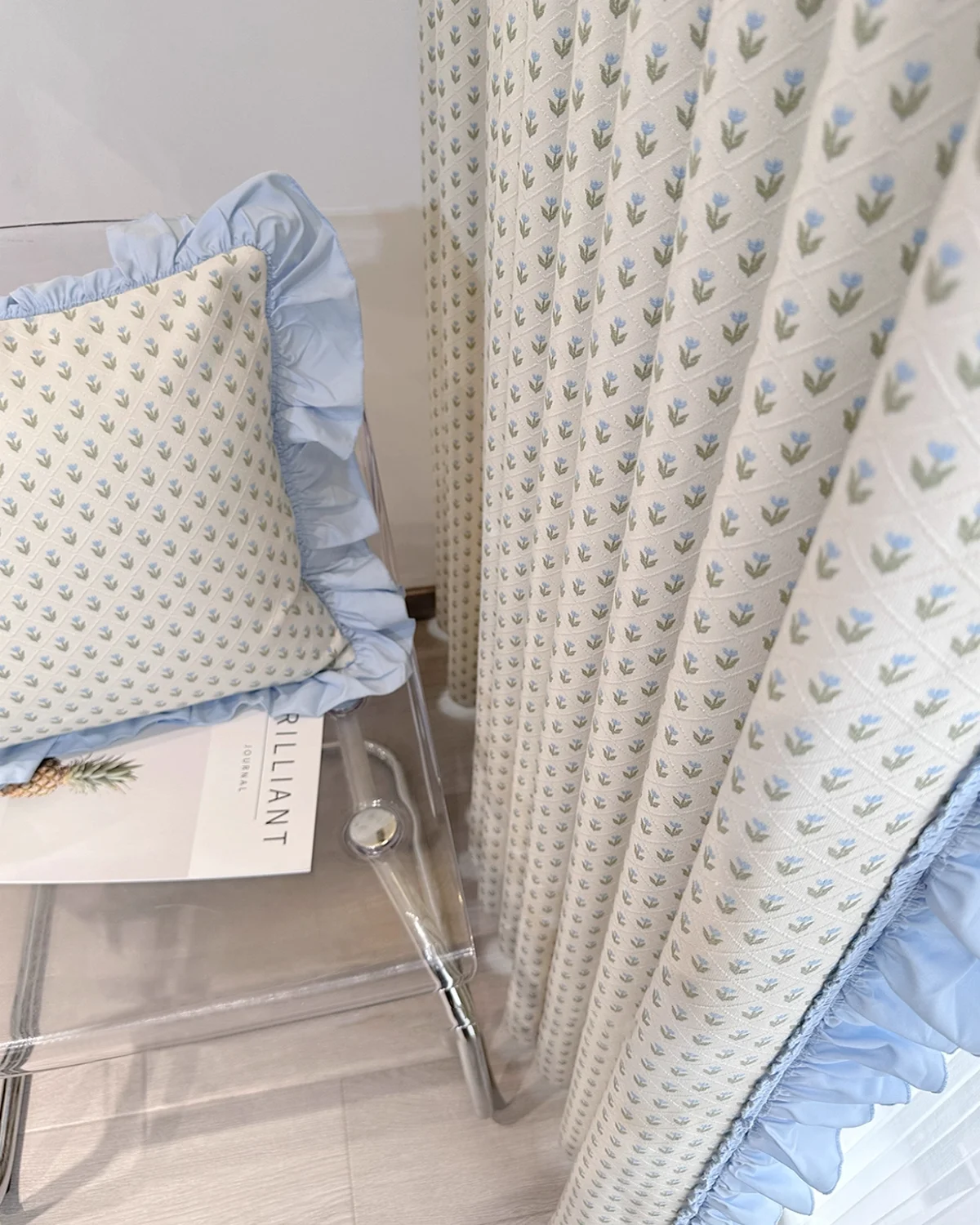 Embroidered sheer curtain styled with matching cushion, showing petite floral pattern and pom pom trim