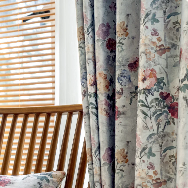 Close-up of botanical print curtains with soft floral design, styled beside wooden chair and window blinds.