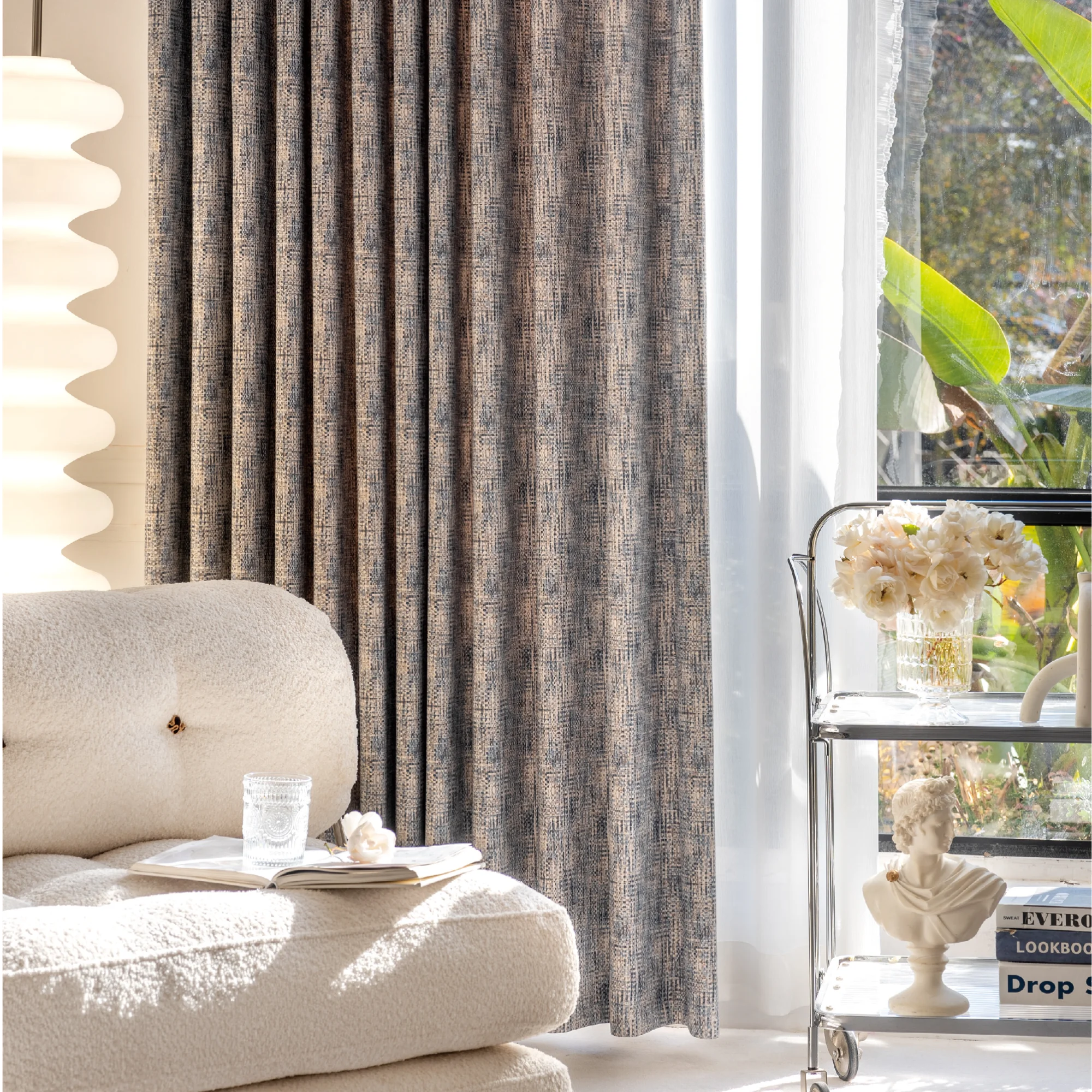 Living room with woven print curtain in deep indigo and beige, styled with neutral sofa and floral decor beside large window
