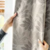 Elegant hand holding taupe botanical jacquard curtain with leaf pattern