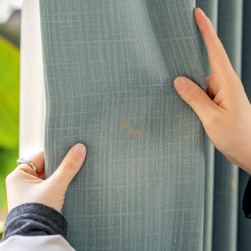 Hand holding green dragonfly weave curtain with subtle embroidery detail.