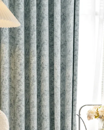 Botanical jacquard curtain in a soft blue tone hanging in a modern living room with wooden lamp and sheer