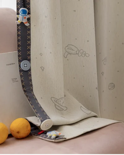 Bottom hem of embroidered kids curtain with planet and star design, shown with toys and sheer fabric lining