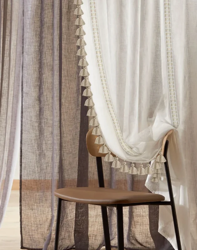 Leather tassel fringe trim on sheer curtain in cozy layered window treatment with warm light and wooden chair