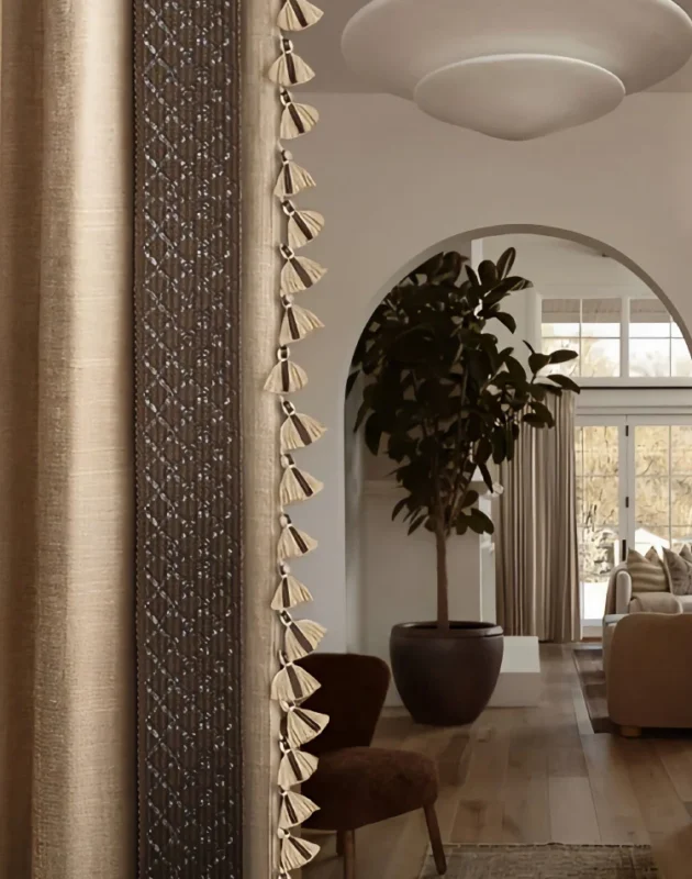 Leather tassel fringe trim on curtain edge in soft-lit modern interior with arched doorway and greenery