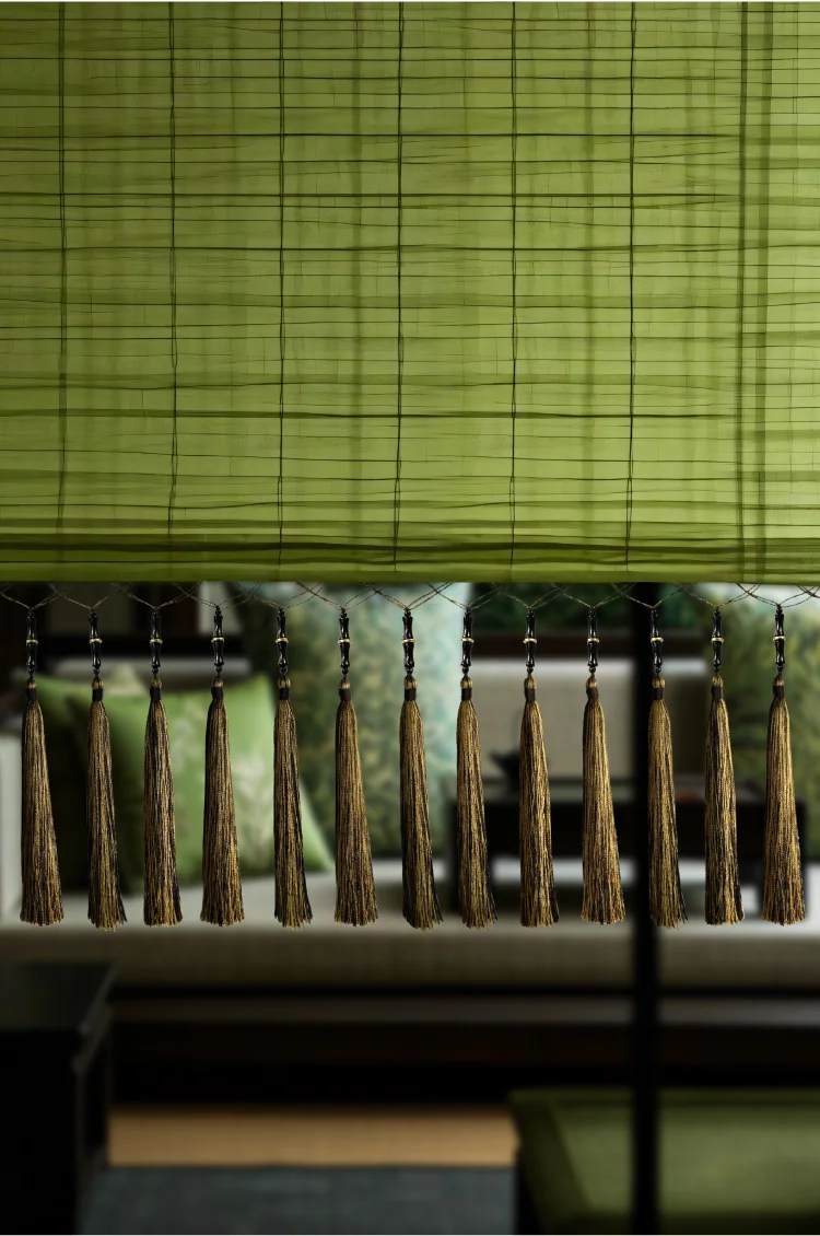 Asian-style curtain with bamboo fringe and moss green tassels, set against bamboo blinds and wooden furniture