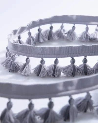 Side-by-side view of single-layer tassel fringe trims in gray blue and beige tones, showing color options