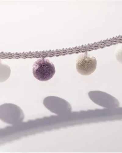 Close-up of lavender and ivory pom pom tassel trim with soft shadows