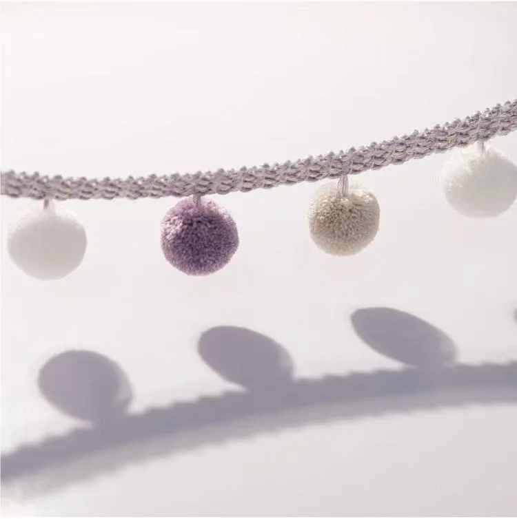 Close-up of lavender and ivory pom pom tassel trim with soft shadows