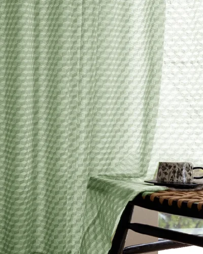 Close-up of green jacquard sheer curtain with geometric pattern next to a table