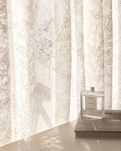 Rope-embroidered floral sheer curtain in warm daylight, light-filtering lace with airy drape by the window.