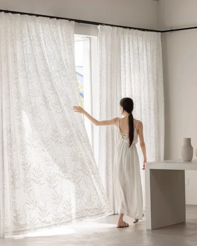 Person opening a rope-embroidered floral sheer curtain in ivory—light-filtering lace with airy drape in a bright living room.