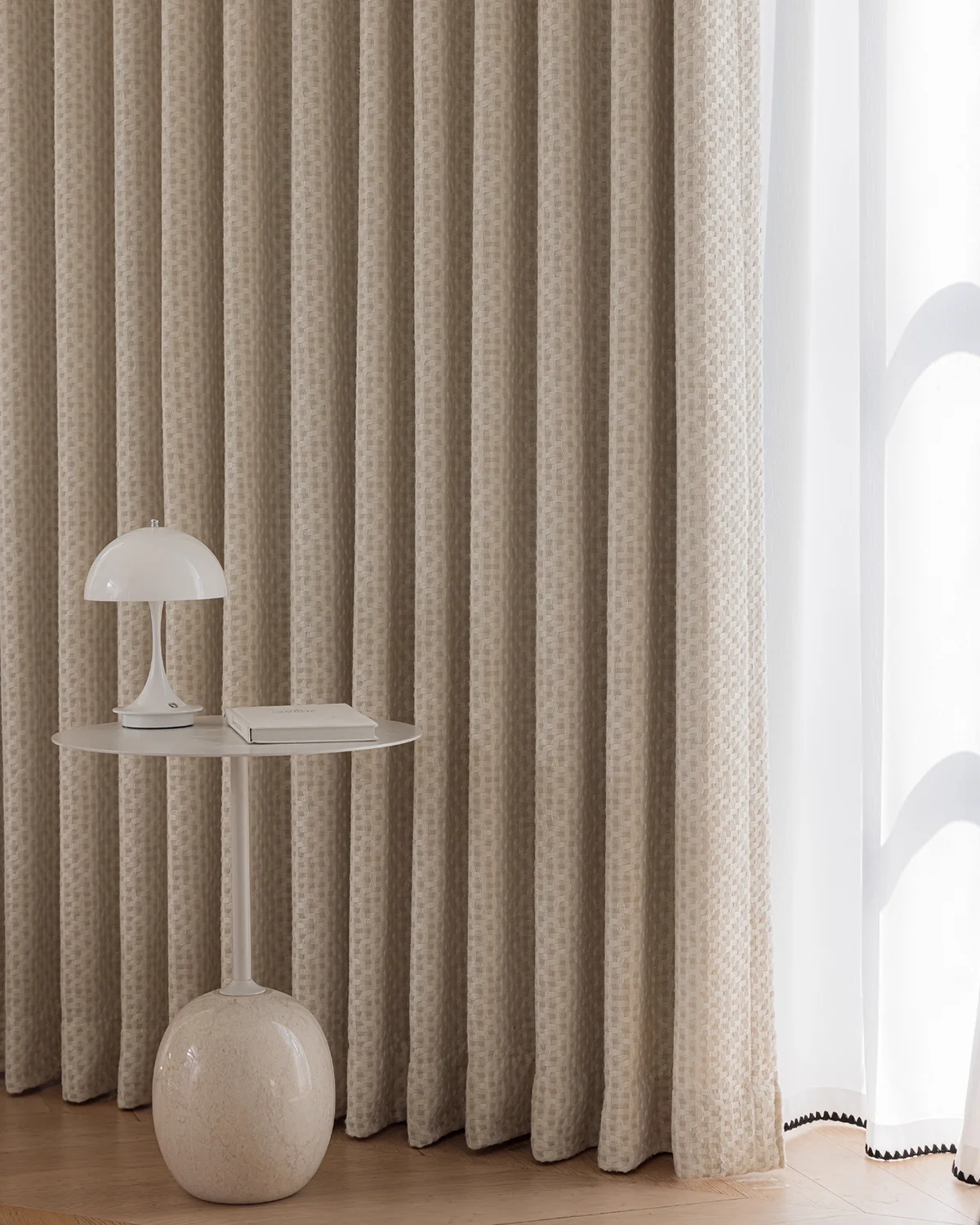 Basketweave texture curtain with soft woven drapes pooling gently on the floor beside a minimalist side table.