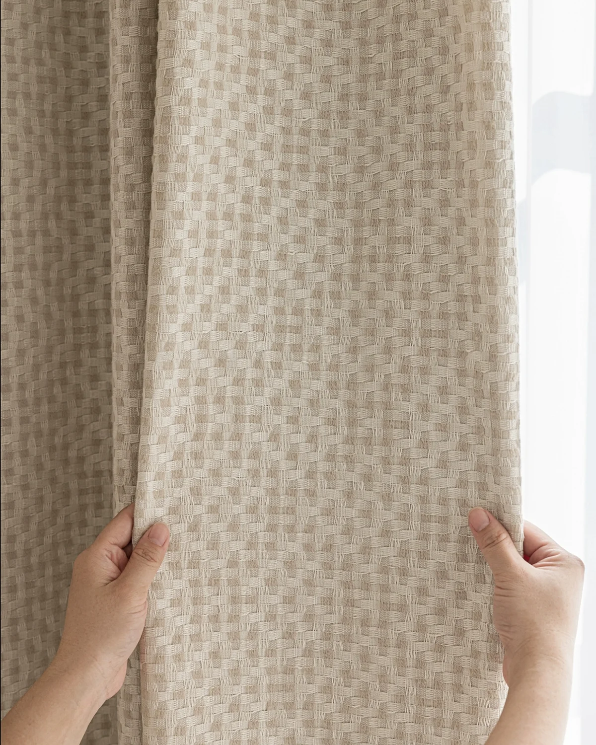 Hands pulling back a basketweave texture curtain, showing the soft woven drapes and tactile fabric surface.
