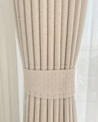 Textured curtain fabric neatly pleated with a wide tieback, lattice texture curtain styling detail.