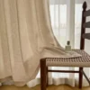 Soft textured curtain fabric hanging by a window next to a wooden chair, showing lattice texture curtain drapes in a modern living room.