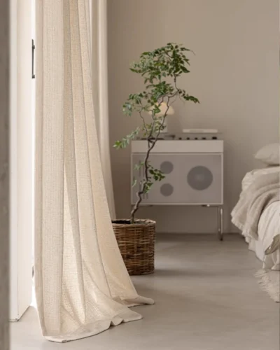 Textured curtain fabric drapes pooling softly on the floor beside a bed and plant, lattice texture curtain for modern bedrooms.