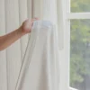 Ridge Texture Curtain – hand holding soft cream textured curtain fabric by the window