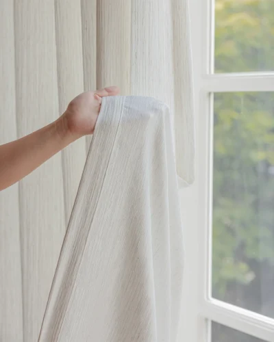 Ridge Texture Curtain – hand holding soft cream textured curtain fabric by the window