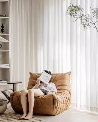 Vertical stripe sheer curtains in soft white voile behind a woman reading in a cozy modern living room.