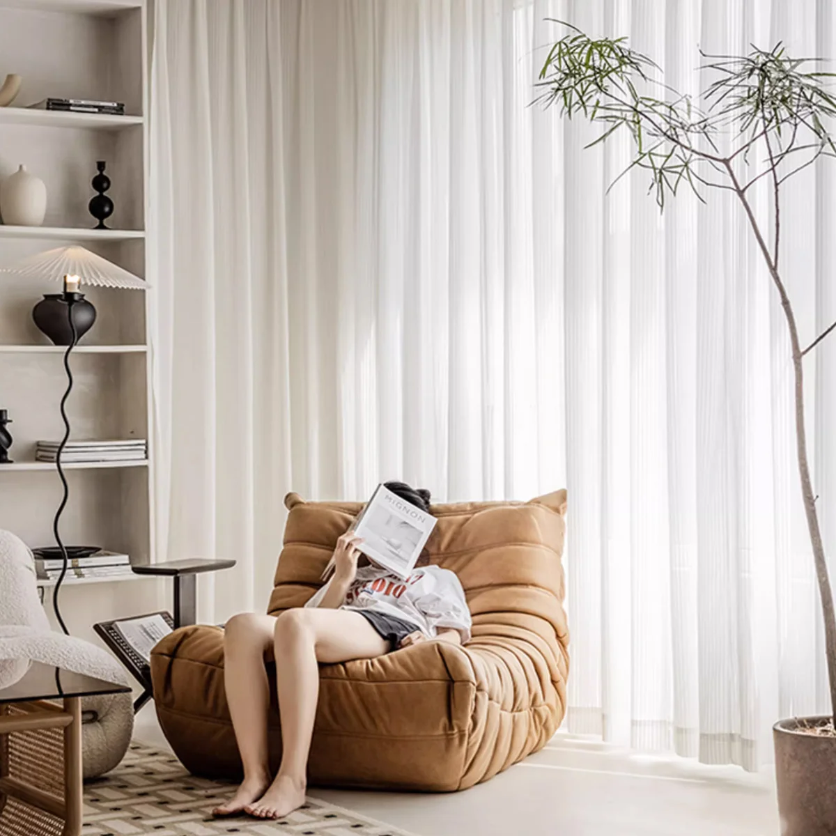 Vertical stripe sheer curtains in soft white voile behind a woman reading in a cozy modern living room.