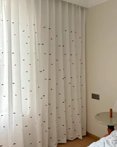 Little Traffic sheer curtain with embroidered cars and buses hanging full height beside a kids room window.