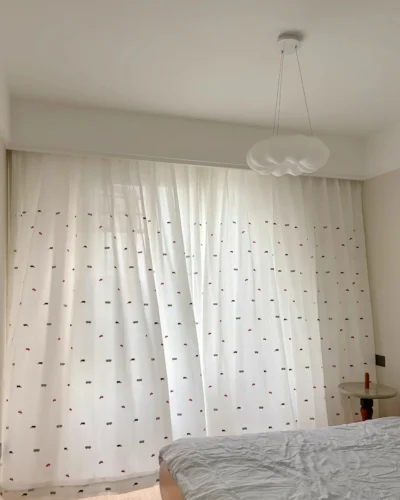 Little Traffic sheer curtain with embroidered cars and buses hanging across a bright kids bedroom window.