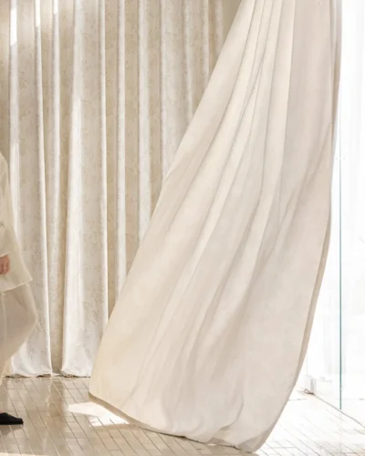 Close-up of Lemonho warm beige floral jacquard curtain fabric, folded in layers to highlight the subtle raised botanical pattern and soft blackout texture.