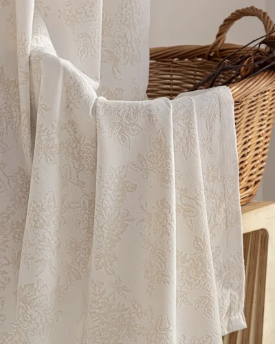 Close-up of warm beige floral jacquard curtain fabric with raised botanical pattern.