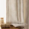 Soft beige floral jacquard curtain hanging by the window with a folded fabric sample on the table.
