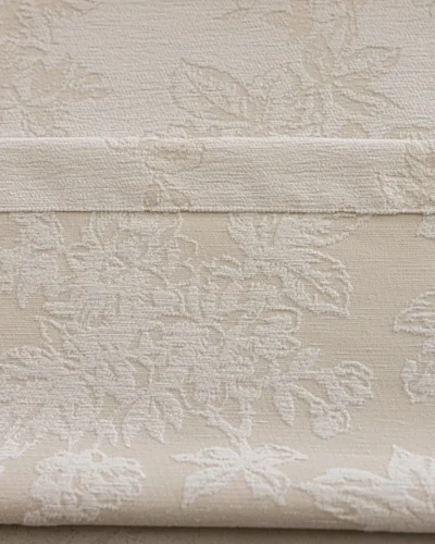 Close-up of warm beige floral jacquard curtain fabric with raised botanical pattern.