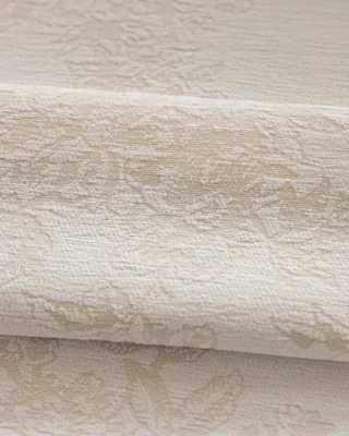 Warm beige floral jacquard curtain fabric folded in soft layers, showing subtle raised pattern.