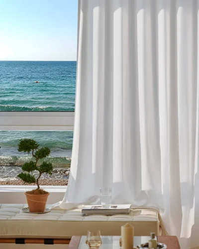 Herringbone sheer curtain in soft white textured voile hanging in front of a large window with ocean view.