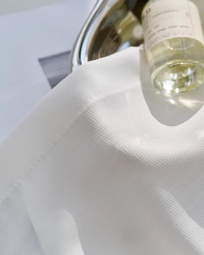 Close-up of soft white herringbone sheer curtain on a window sill with a glass bottle.