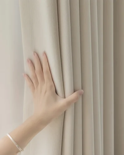 Hand touching beige blackout curtains beside sheer white drapes