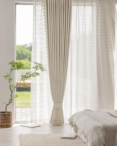 Bedroom with floor-to-ceiling Confetti Pom Pom Curtains in a multicolour dotted weave, soft light filtering onto a white bed beside the window.