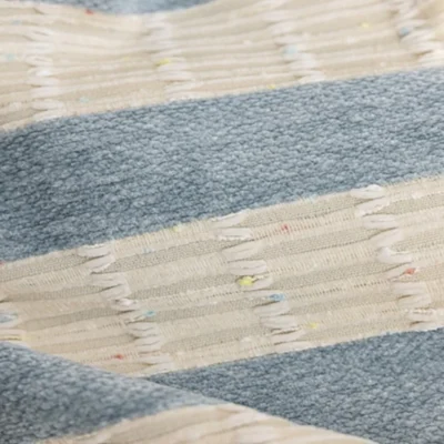 Blue-grey and cream striped curtain fabric close-up with confetti speckles and fringe texture