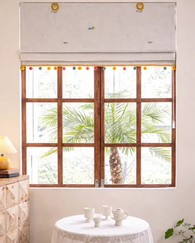 Whimsical safari Roman shade with colorful pom-pom trim on a wooden window, styled in a bright kids room.