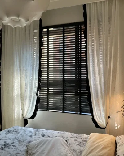 Black wooden venetian blinds in a cosy bedroom with white curtains