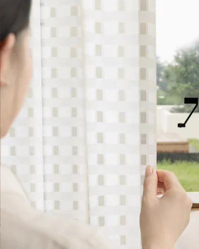 Hand touching the Ivory Grid Sheer Curtain to show its soft light-filtering texture and subtle geometric pattern