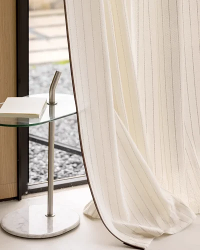 Hand touching the Mocha Pinstripe Sheer Curtain to show its soft texture, flowing drape, and mocha edge detail