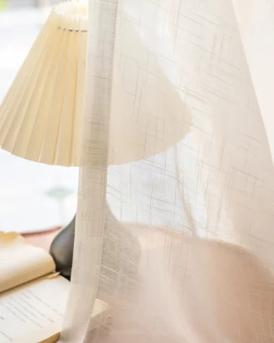 Soft linen texture sheer curtain with white natural weave fabric and soft light filtering effect beside a table lamp
